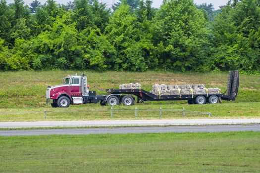 Horizontal side shot of a flatbed 18-wheeler going down the highway carrying a load of stone for construction.