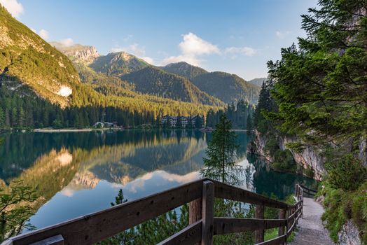 A path with a wooden fence climbs steeply beside the Braies lake, mountain landscape in South Tyrol