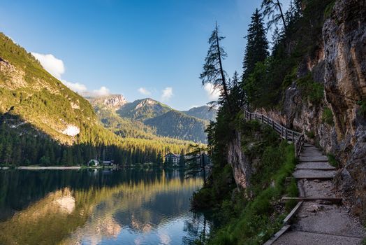A path with a wooden fence climbs steeply beside the Braies lake, mountain landscape in South Tyrol
