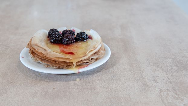 Stack of thin pancakes poured with honey and decorated with fresh blueberries side view with selective focus. The concept of Russian holiday Maslenitsa