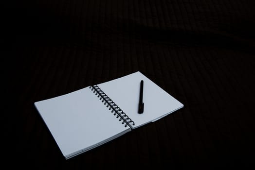 open spiral notebook to point with a pen on a dark background