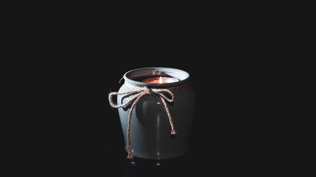 Candle burns in a vase on an isolated black background with empty place for text