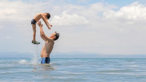 Happy european family playing at the sea. Dad and little son play and enjoy the sea water on the shore of lake, sea or ocean. Family vacation. Family tours, trips. Father playing with son at sea shore