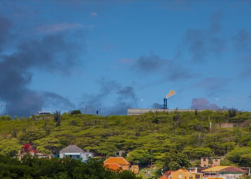 A Burning Refinery Tower on Curacao Beyond City and Greenery