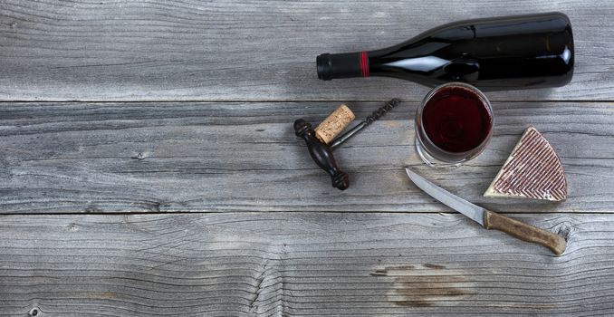 Fresh cheese wedge and red wine in a glass on rustic wood 