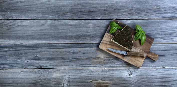 Fresh cheese wedge with basil leaves on rustic wood with copy space available 