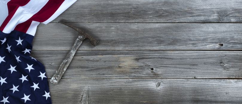 Vintage construction hammer with waving US Flag on rustic wooden background with copy space