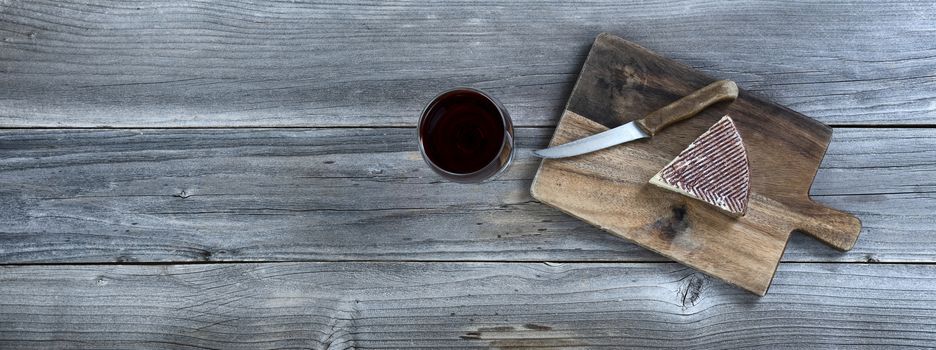 Fresh cheese wedge on cutting board with red wine in a glass on rustic wooden table 