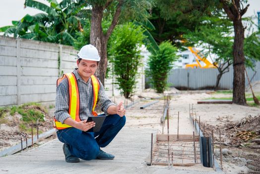 Asian man civil construction engineer worker or architect with helmet and safety vest working and holding a touchless tablet computer for see blueprints or plan at a building or construction site