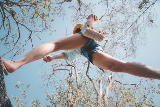 Low angle view of sexy woman short jeans midair by jumping, crossing step over camera shot below in forest with tree and sky overhead in concept travel, active lifestyle, overcome obstacles in life