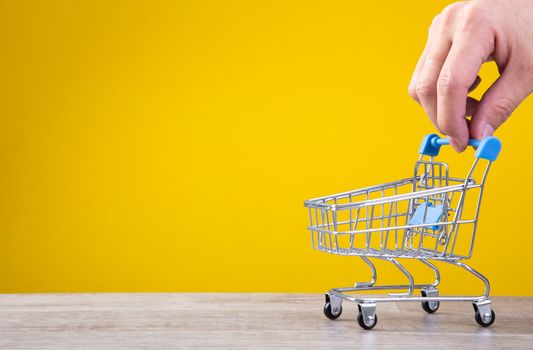 Buying things at market shops concept. hand with tiny shopping cart.