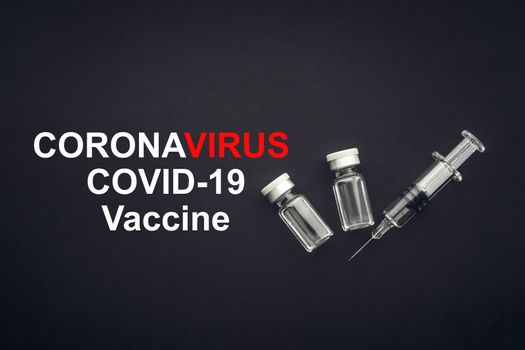 CORONAVIRUS COVID-19 VACCINE text with syringe and vials on black background. Covid-19 and Coronavirus concept