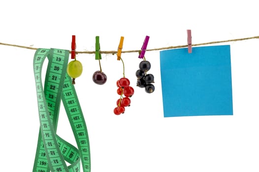 Fresh fruit, tape measure and blank sticky note hanging from clothes pegs on a rope with a gooseberry, red currants, cherry and black currants in a healthy diet concept