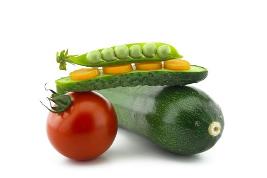 Healthy fresh vegetable still life over white with ripe red tomatoes, courgette or zucchini, carrots, peas in a pod and cucumber balance on top of each other
