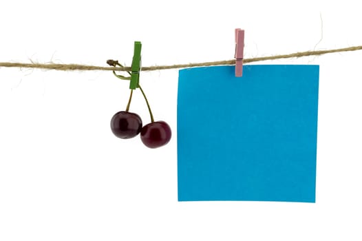 Fresh fruit and and blank sticky note hanging from clothes pegs on a rope with a red cherry and black currants isolated on white with copyspace