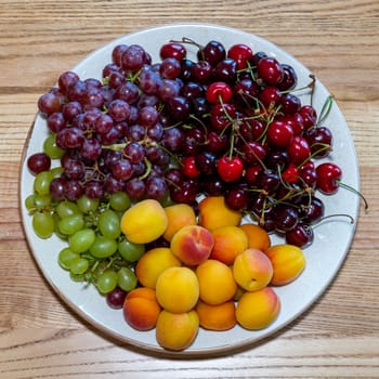 Fresh fruits on a plate. Fruit still life. Dish of fresh fruit. Grapes, cherries and peach on a plate