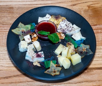 Farm cheeses. Three types of cheese and sauce on a black plate