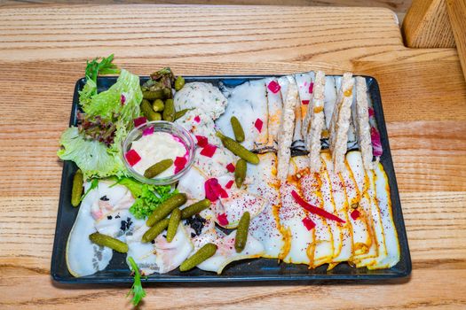 Sala Quartet. Four types of lard. Lard, canned cucumbers, spices, sauce, lettuce. Black square plate on a light wooden table