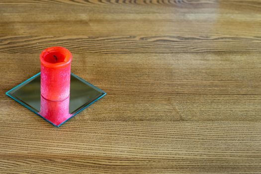 A thick red candle stands on the table. Side view. Place for text