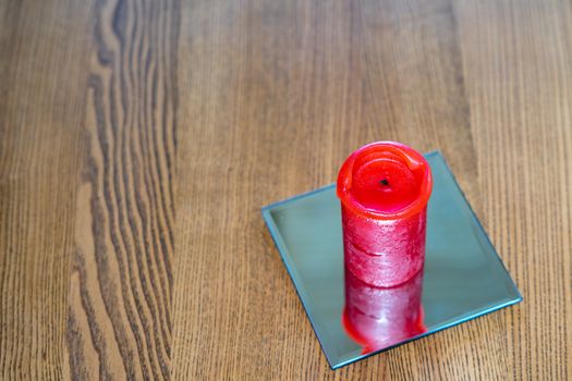 A thick red candle stands on the table. Side view. Place for text