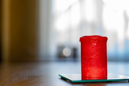 A thick red candle stands on the table. Side view. Place for text