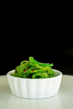 Japanese food concept. Fresh seaweed salad with sesame seeds in white bowl on black background.