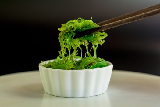 Japanese food concept. Fresh seaweed salad with sesame seeds in white bowl with chopstick on black background.