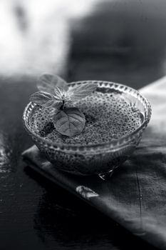 Close up of soaked sabja seeds or falooda seeds or sweet basil seeds in a glass bowl on brown colored napkin on wooden surface with some mint leaves in it.Used in many flavored beverages.