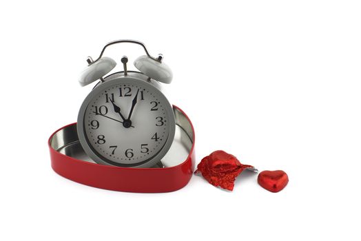 Retro alarm clock in a red heart shaped box with chocolate candy alongside on a white background with copyspace symbolic of love, togetherness and romance for Valentines