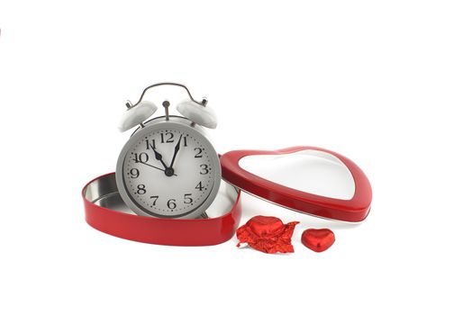 Retro alarm clock in a red heart shaped box with chocolate candy alongside on a white background with copyspace symbolic of love, togetherness and romance for Valentines