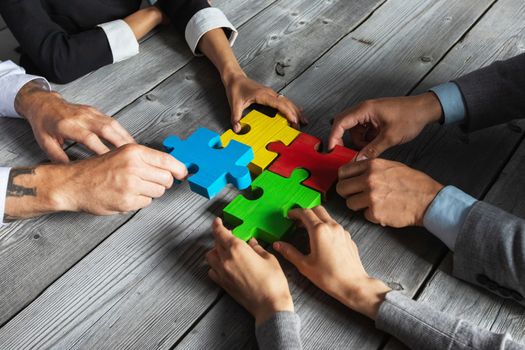 Business people team sitting around meeting table and assembling color jigsaw puzzle pieces unity cooperation ideas concept