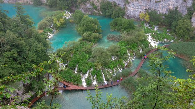 Tourists on the wooden park pathways enjoying the view of emerald lakes, cascades and crystal clear water, Plitvice Lakes National Park, Croatia.