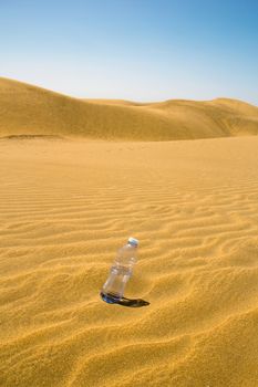 plastic bottle of water in the sand of the desert with blue sky