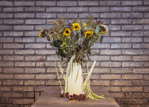 Looking slightly down at a vase of dying flower arrangement, large once bright now dying sun flowers in a vase on a very large marble dining table