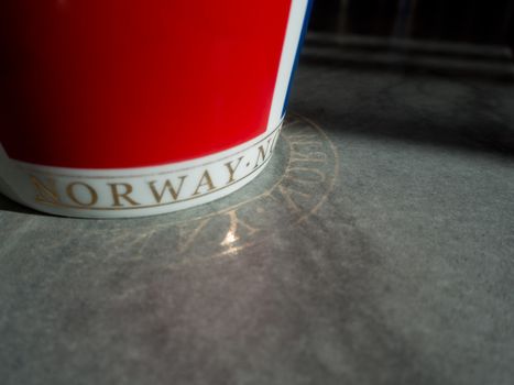 Red cup with Norwegian text reflected on the floor.