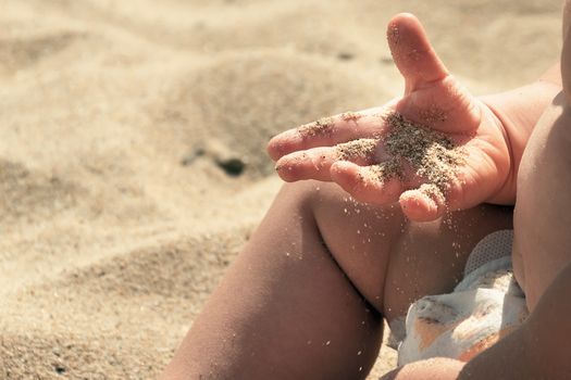 Sand in baby hands. Child playing with beach sand. He has for the first time golden grains of sand in his hands. Infant boy is delight because of learning and discover world with satisfaction and joy.