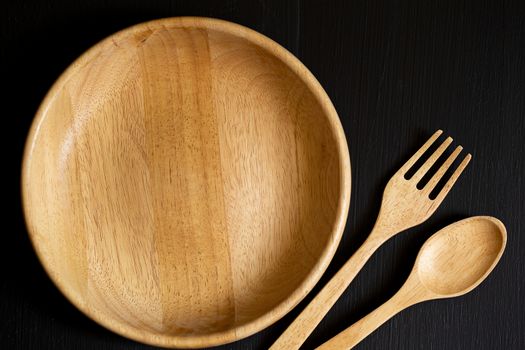 Spoons, forks and Dish made of wood on the black wooden background.