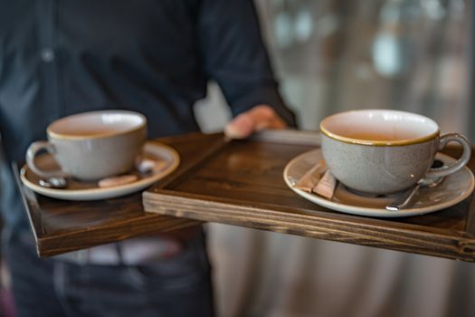 Cups of cappuccino in hands. Serving coffee in a restaurant, bar, cafe. At the wedding reception, at the birthday party, at the meeting, at the important meeting.