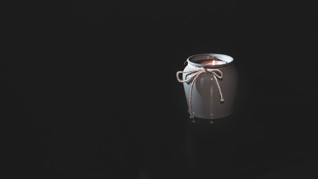 Candle burns in a vase on an isolated black background with empty place for text