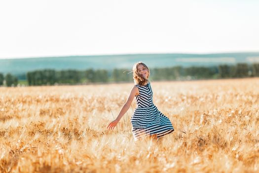 Happy teenage beautiful girl running down golden wheat field at the sunset