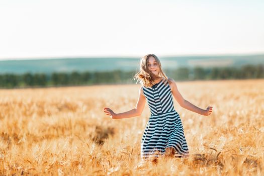 Happy teenage beautiful girl running down golden wheat field at the sunset