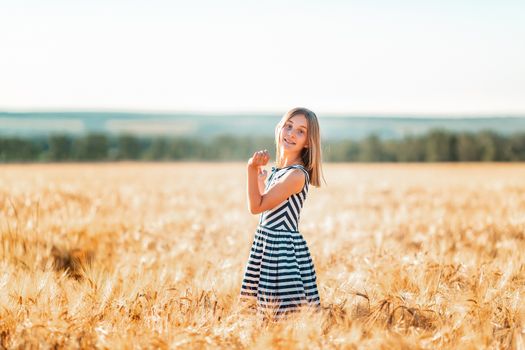 Happy teenage beautiful girl running down golden wheat field at the sunset