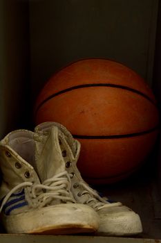 Close up pair of old worn sport sneakers shoes and one basketball ball in locker, low angle view