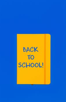 Back to school handwritten sign on yellow leather cover notebook over blue paper background with copy space