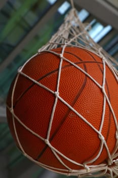 Close up one basketball ball hanging in mesh sack, low angle side view