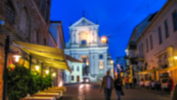 Blurred background. Evening city landscape, city street with lights and passers-by. Creative story for a background, poster, banner, or screensaver.
