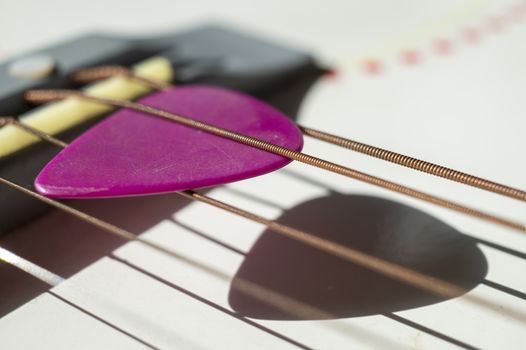 Colorful pink plectrum in guitar strings in a close up oblique angle view in a music and entertainment concept