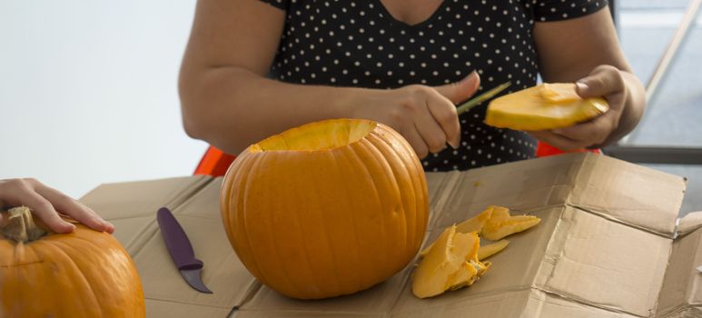 Process of carving pumpkin to make Jack-o-lantern. Creating traditional decoration for Halloween and Thanksgiving. Cutted orange pumpkin lay on table in woman hands