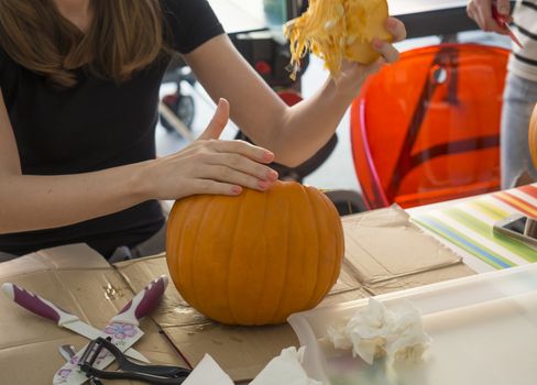 Process of carving pumpkin to make Jack-o-lantern. Creating traditional decoration for Halloween and Thanksgiving. Cutted orange pumpkin lay on table in woman hands