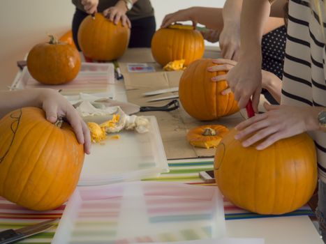 Group of people carving pumpkin to make Jack-o-lantern. Creating traditional decoration for Halloween and Thanksgiving. Cutted orange pumpkin lay on table